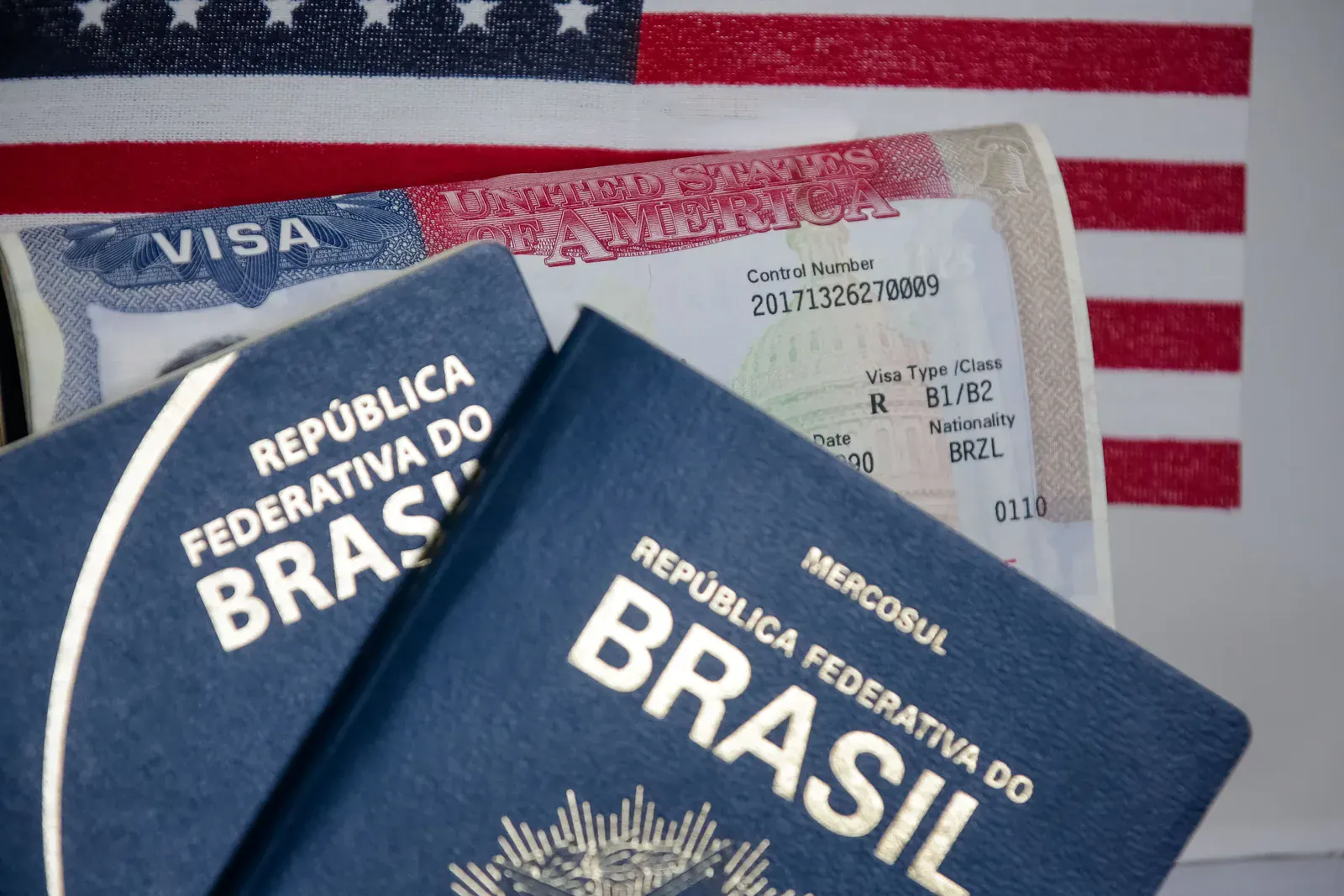 Passaportes brasileiros sobre um visto americano B1/B2, com a bandeira dos Estados Unidos ao fundo